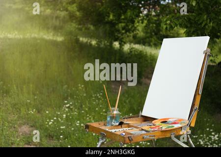 Staffelei mit leerer Leinwand und Malmaschinen in malerischer Landschaft Stockfoto