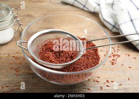 Sieb mit braunem Reis in der Schüssel auf einem Holztisch Stockfoto