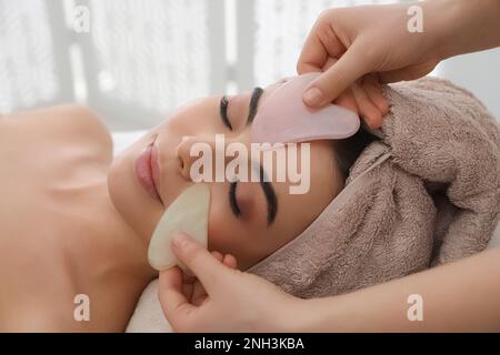 Junge Frau, die im Schönheitssalon eine Gesichtsmassage mit Gua-sha-Werkzeugen erhält Stockfoto