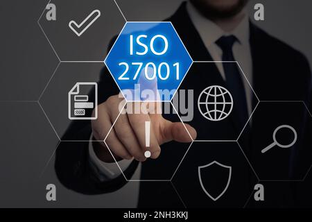 Geschäftsmann, der auf ein virtuelles Symbol zeigt, mit Text ISO 27001 auf dunklem Hintergrund, Nahaufnahme. Qualitätsmanagementsystem Stockfoto
