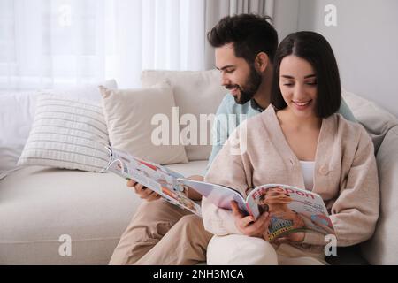 Junges Paar liest zu Hause moderne Zeitschriften auf dem Sofa, Platz für Text Stockfoto