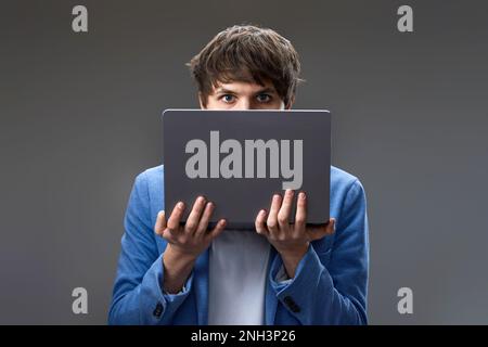 Ein junger Mann versteckt sein Gesicht mit einem Laptop Stockfoto