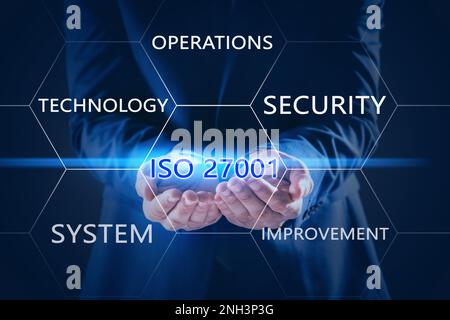 Geschäftsmann, der Text ISO 27001 auf dunklem Hintergrund vorführt, Nahaufnahme Stockfoto