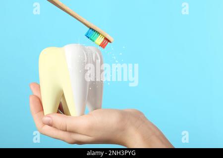 Frau mit Keramikmodell von Zahn und Holzpinsel auf hellblauem Hintergrund. Das Whitening-Konzept Stockfoto