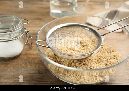 Sieb mit Reis in der Schüssel auf einem Holztisch Stockfoto