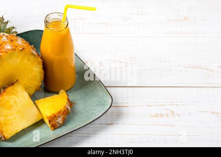 Scheiben saftiger Ananas und ein frischer, gesunder Smoothie in einer Glasflasche und ein Strohhalm auf einer grünen Platte auf Holzhintergrund. Gesund, Entgiftung und Dieta Stockfoto