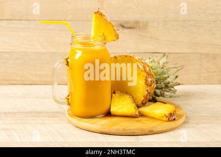 Scheiben saftiger Ananas und ein frischer, gesunder Smoothie in einer Glasflasche und einem Strohhalm auf einem Holzbrett auf Holzhintergrund. Gesund, Entgiftung Stockfoto