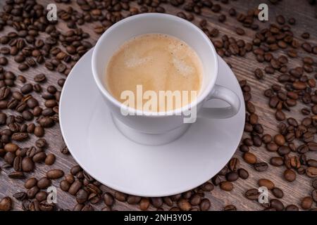 Kaffeecrema in einer weißen Tasse mit Kaffeebohnen im Hintergrund Stockfoto