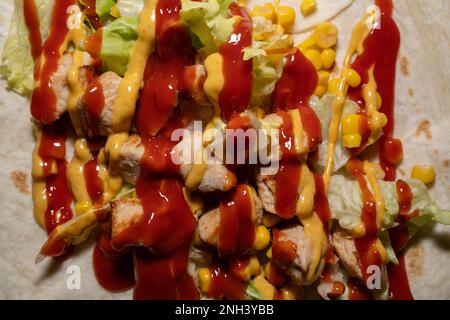 Nahaufnahme eines Wickels mit Salat, Zuckermais, Huhn, Ketchup und Senfsauce Stockfoto