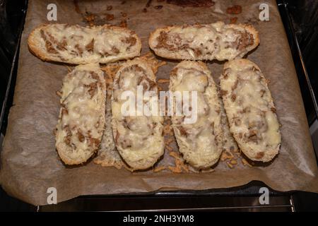 Knusprig gebackene Thunfischsandwiches mit geschmolzenem Käse auf einem Backblech mit Pergamentpapier Stockfoto