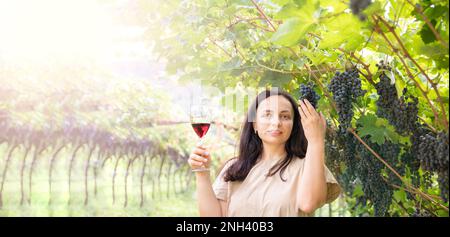 Wunderschöne Frau träumt von Rotwein und genießt den Sommeraufenthalt in Weinbergen an einem schönen sonnigen Tag. Eine Frau, die Rotwein trinkt. Erntesaison. Hochwertiges Foto Stockfoto