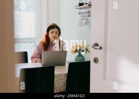 Porträt einer gelangweilten jungen Frau mit Kopfhörern, die zu Hause auf einem Laptop arbeiten Stockfoto