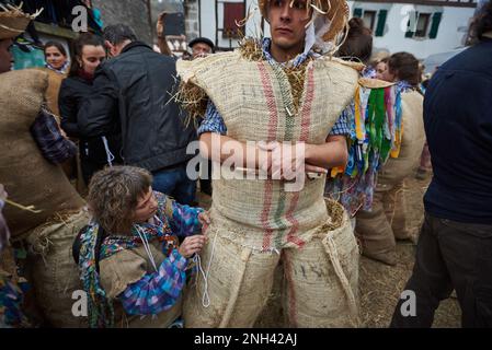 Lesaka, Spanien. 18. Februar 2023. Ein „zaku-zaharrak“ wird von einer „Mairuak“ (Frauen in Bändern) zubereitet, während sie das zaku-Kostüm mit Seil auf dem Karneval von Lesaka näht. Der „zaku-zaharrak“ sind typische Figuren des Lesakakaker Karnevals, gefüllt in Säcke voller Stroh mit Gesichtern bedeckt mit Schals, die aufgeblasene Blasen tragen, um die Menschen zu treffen, die bei Sonnenuntergang durch die Straßen der Stadt laufen. Kredit: SOPA Images Limited/Alamy Live News Stockfoto