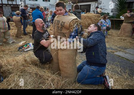 Lesaka, Spanien. 18. Februar 2023. Ein Kind, das als "zaku-zaharrak" getarnt ist, die Männer des alten Sacks gefüllt mit Stroh, wird von Männern während des Karnevals von Lesaka vorbereitet. Der „zaku-zaharrak“ sind typische Figuren des Lesakakaker Karnevals, gefüllt in Säcke voller Stroh mit Gesichtern bedeckt mit Schals, die aufgeblasene Blasen tragen, um die Menschen zu treffen, die bei Sonnenuntergang durch die Straßen der Stadt laufen. Kredit: SOPA Images Limited/Alamy Live News Stockfoto