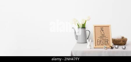 Rahmen, Nest mit Ostereiern, Tulpen und Kaninchen auf einem Tisch nahe der weißen Wand Stockfoto
