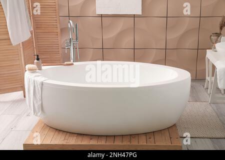 Die Innenausstattung des Badezimmers ist mit moderner Badewanne, Faltschirm und Handtüchern ausgestattet Stockfoto