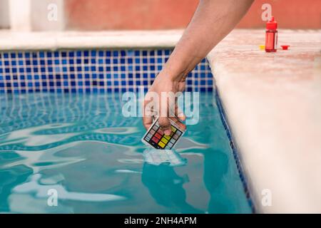 Nahaufnahme der Person, die den ph-wert des Wassers mit einem Minitester im Schwimmbad testet. Manuelle Prüfung des Poolwassers auf Chlor mit dem PH-Minitester. Test Stockfoto