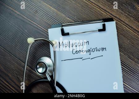 Zum Konzept des Molluscum contagiosum-Schreibens auf Unterlagen mit auf Holztisch isoliertem Stethoskop. Stockfoto