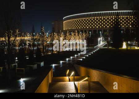 Russland, Krasnodar - 04. Januar 2023: Wunderschöne Nachtbeleuchtung des Krasnodar-Stadions und des Galicischen Parks. Girlanden auf den Bäumen Stockfoto
