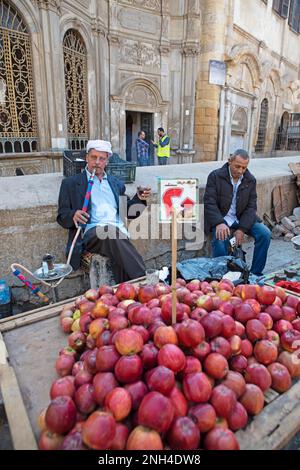 Ein ägyptischer Mann, der an einem Obststand Shisha oder Wasserpfeife raucht, in der Altstadt, in Kairo, Ägypten Stockfoto