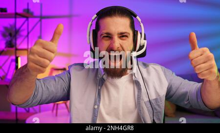 Ein bärtiger Gamer in einem Gaming-Headset gewinnt ein Videospiel. Cybersportler in einem Neonraum. Lifestyle-Gamer, Online-Spiele. Sieg im E-Sport Stockfoto