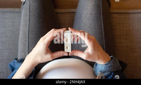 Draufsicht einer schwangeren Frau mit positivem Testergebnis mittels Schnelltestgerät für COVID-19 Stockfoto
