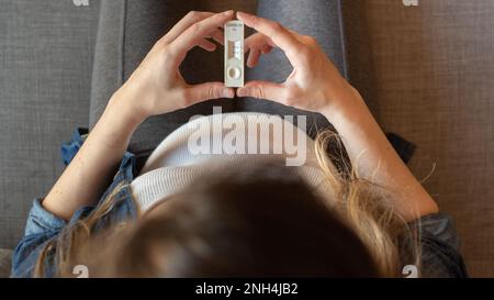 Draufsicht einer schwangeren Frau mit positivem Testergebnis mittels Schnelltestgerät für COVID-19 Stockfoto