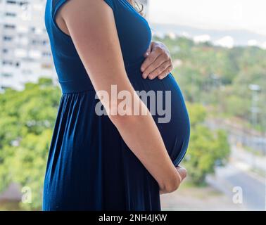 Schwangere Frau, die ihren Bauch vor einem Stadtbild hält Stockfoto