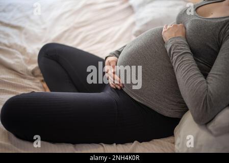 Schwangere Frau auf dem Bett sitzend Stockfoto