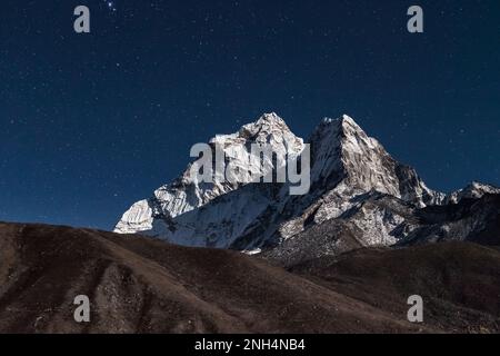 Der Gipfel des AMA Dablam Mountain wird bei hellem Mondlicht in einer Sternennacht beleuchtet. Wunderschöne nächtliche Berglandschaft bei hellem Mondlicht. Sterne über Himala Stockfoto