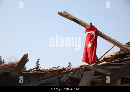 Die türkische Fahne hing auf einer Holzsäule, die sich nach den Trümmern eines zerstörten Gebäudes nach den mächtigen Kahramanmaraş-Erdbeben erhebte. Stockfoto