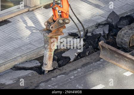 Baumaschine bricht einen Graben auf einer Straße und bohrt ihn zur Reparatur. Großer pneumatischer Hammer, der auf dem Hydraulikarm einer konstruktionsmanschette montiert ist Stockfoto