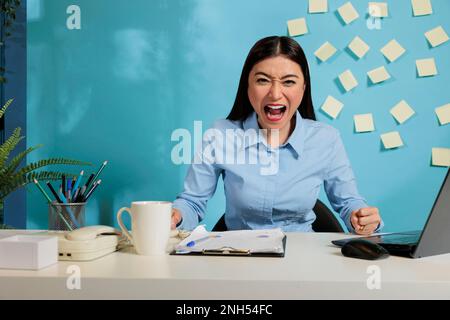 Überarbeitete weibliche Mitarbeiterin, die Verzweiflung und Stress ausdrückt, indem sie laut in die Kamera schreit. Berufstätige Frau mit negativen Gefühlen durch übertriebene Arbeitsbelastung. Stockfoto