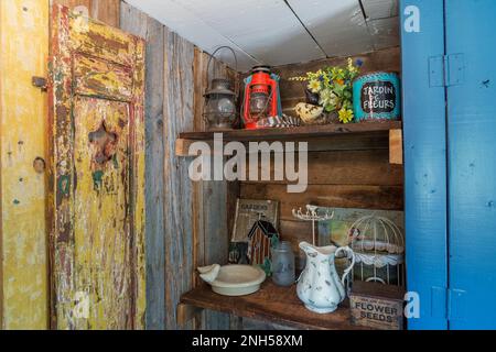 Vintage-Objekte wie antike Öllampen in den Regalen in der Erweiterung mit einer Stallenholzwand im alten 1841 Jahre alten Feldsteinhaus. Stockfoto