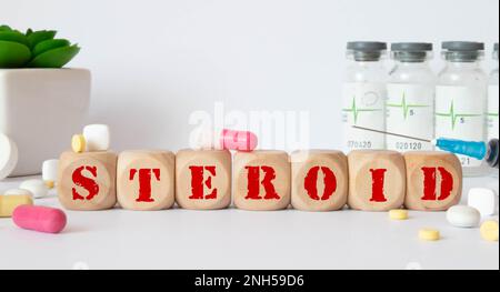 Wort STEROID aus Holzbuchstaben auf grauem Hintergrund. Pflanzen im Hintergrund. Medizinisches Konzept Stockfoto