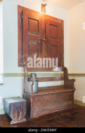 Antike Holzsitzbank und Aufbewahrungsbank in der Ecke des Esszimmers mit Bunttteeböden in einem alten Haus aus Feldsteinen aus dem Jahr 1841. Stockfoto