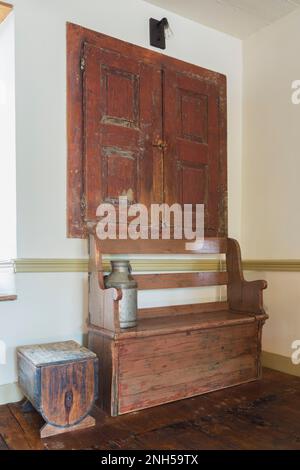 Antike Holzsitzbank und Aufbewahrungsbank in der Ecke des Esszimmers mit Bunttteeböden in einem alten Haus aus Feldsteinen aus dem Jahr 1841. Stockfoto