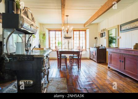 Antiker Belanger 'Major'-Holzofen und roter fleckiger antiker Holztisch und Kiefernholzstühle, Buffet im Speisesaal. Stockfoto