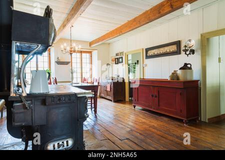 Antiker Belanger 'Major'-Holzofen und roter fleckiger antiker Holztisch und Kiefernholzstühle, Buffet im alten Speisesaal. Stockfoto