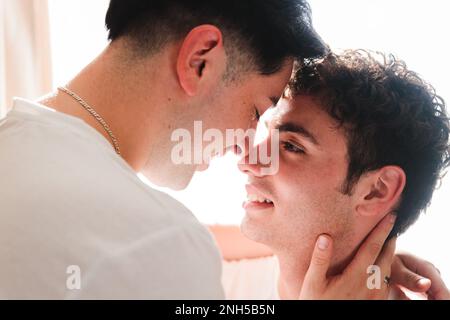 Nahaufnahme eines schwulen Paares, das sich romantisch auf den Mund küsst, im Wohnzimmer. LGBT-Beziehungsroutine. Stockfoto