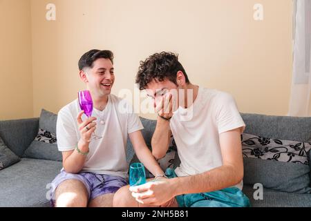 Ein lateinamerikanisches schwules Paar, das mit Weingläsern anstoßen und lachen will, um seinen Jahrestag zu feiern Stockfoto