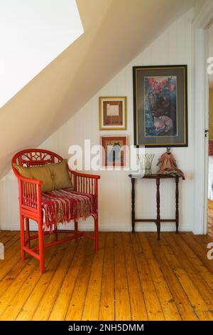 Antiker roter Holzsessel und Konsolentisch neben weißer Lattenwand im oberen Flur mit Holzfußboden im alten Haus aus dem Jahre 1830. Stockfoto