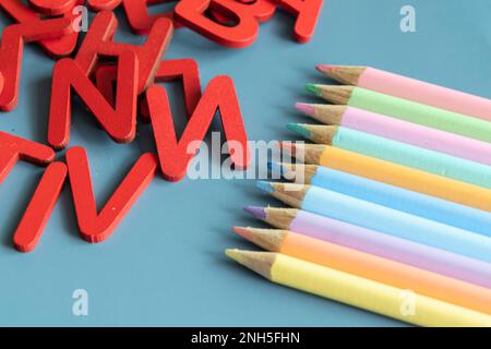 Back-to-School-Konzept mit verschiedenen Buchstaben und Buntstiften in Pastellfarben auf blauem Hintergrund Stockfoto