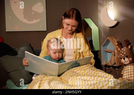 Mutter und Kind lesen Buch im Zimmer mit sichelförmiger Nachtlampe Stockfoto