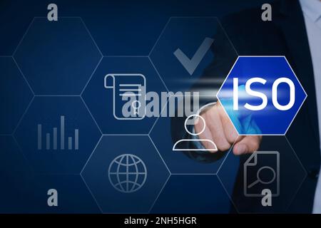 Geschäftsmann, der auf ein virtuelles Symbol zeigt, mit Text-ISO auf dunklem Hintergrund, Nahaufnahme Stockfoto