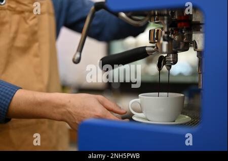 Zugeschnittenes Bild eines professionellen männlichen Baristas, der einen Espresso Shot mit einer Espressomaschine zubereitet, Kaffeebestellungen vorbereitet und im Café arbeitet. Stockfoto