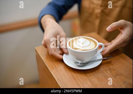 Nahaufnahme eines männlichen Baristas, der einem Gast am Tisch einen schönen Latte serviert. Café-Bar oder Café-Konzept Stockfoto