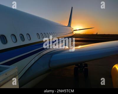 Silhouette eines Passagierflugzeugs, das vor dem malerischen orangefarbenen Sonnenuntergang auf der Flughafenschürze landet Stockfoto