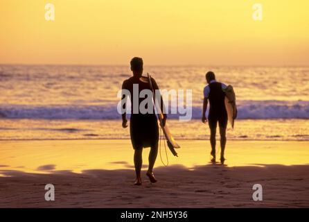 Surfer, die bei Sonnenuntergang an der Küste Südkaliforniens ins Wasser kommen. Stockfoto