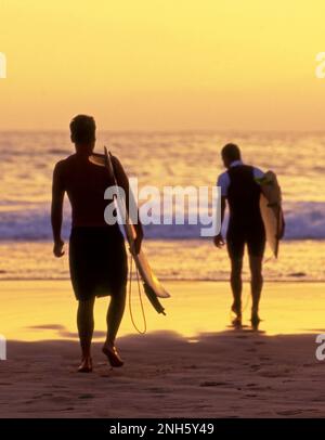 Surfer, die bei Sonnenuntergang an der Küste Südkaliforniens ins Wasser kommen. Stockfoto